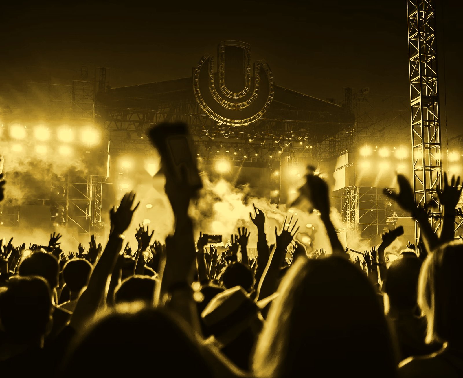 A crowd with hands raised in front of a lit concert stage